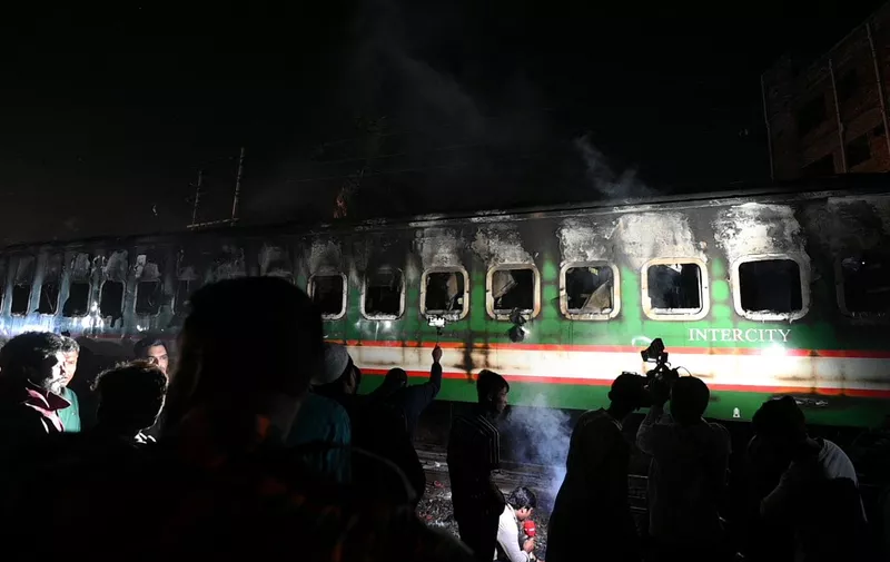On lookers gather as Bangladeshi fire fighters search the burnt out carriages of the Benapole Express in Dhaka on January 5, 2024. Five people were killed in Bangladesh after a passenger train which was arriving in the capital Dhaka from the western city of Jessore, caught fire on January 5, 2024, with police suspecting an arson attack during unrest ahead of national elections boycotted by the opposition. (Photo by Munir uz zaman / AFP)