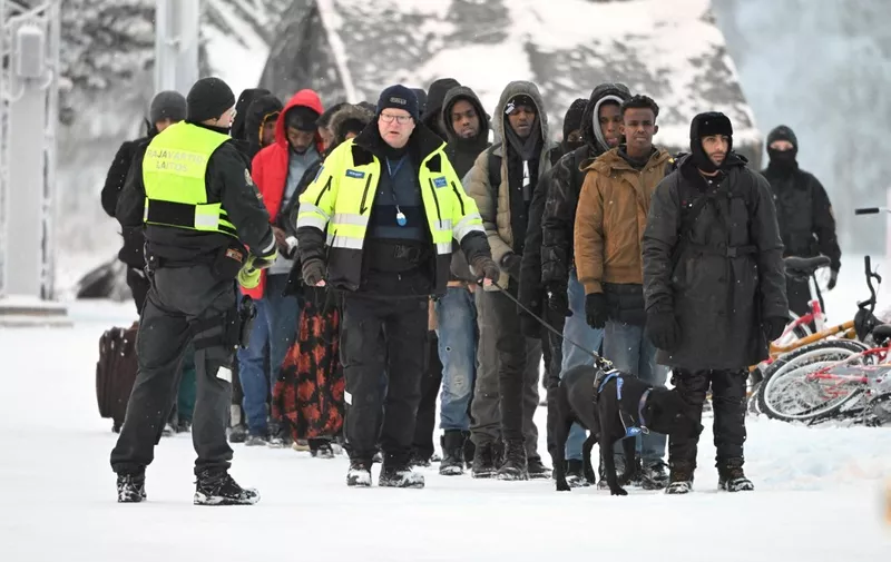 A Finnish border guard and a customs officer with dog escort a group of migrants at the international border crossing at Salla, Finnish Lapland, on November 23, 2023. Russia announced tightened security in its northern Murmansk region after Finland said it would close all but one border crossing between the two countries. Helsinki said on November 22, 2023 the move follows a surge in attempted crossings by migrants seeking asylum in the EU country -- which Finland says is a destabilisation ploy by Russia. (Photo by Jussi Nukari / Lehtikuva / AFP) / Finland OUT