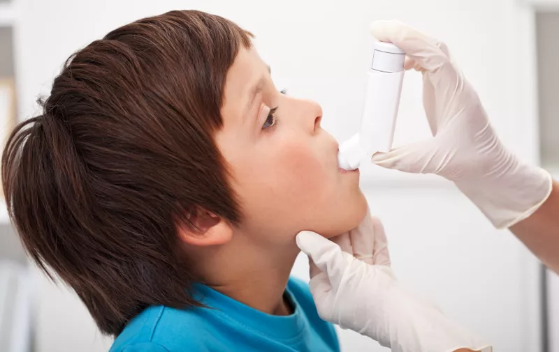 Boy with respiratory system illness receiving help using an inhaler