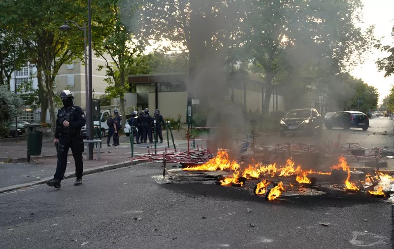 Police in riot gear stand next to a fire burning in the street  after a demonstration in Nanterre, west of Paris, on June 27, 2023, after French police killed a teenager who refused to stop for a traffic check in the city. The 17-year-old was in the Paris suburb early on June 27 when police shot him dead after he broke road rules and failed to stop, prosecutors said. The event has prompted expressions of shock and questions over the readiness of security forces to pull the trigger. (Photo by Zakaria ABDELKAFI / AFP)