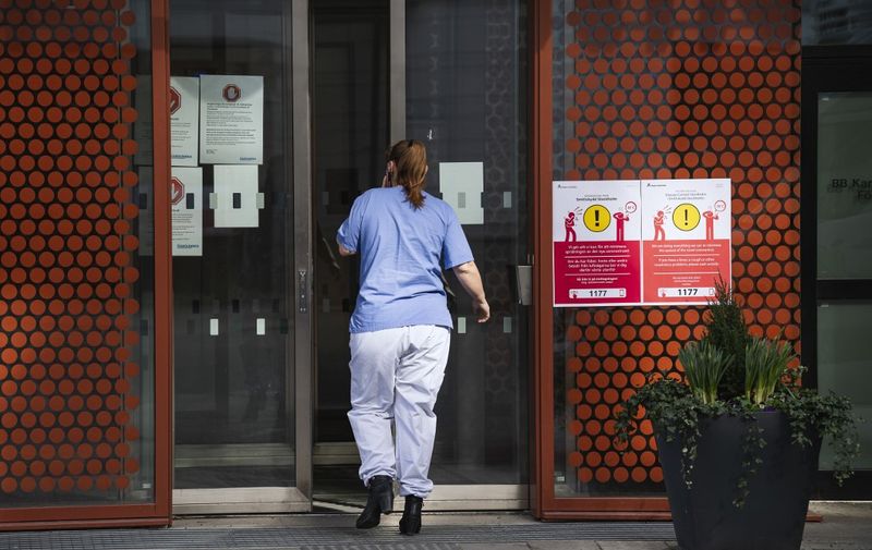 A medical worker walks in the entrance, with an information sign to help minimising the spread of the novel coronavirus COVID-19 hung up, at Karolinska Hospital in Solna, Sweden, on March 31, 2020. (Photo by Jonathan NACKSTRAND / AFP)
