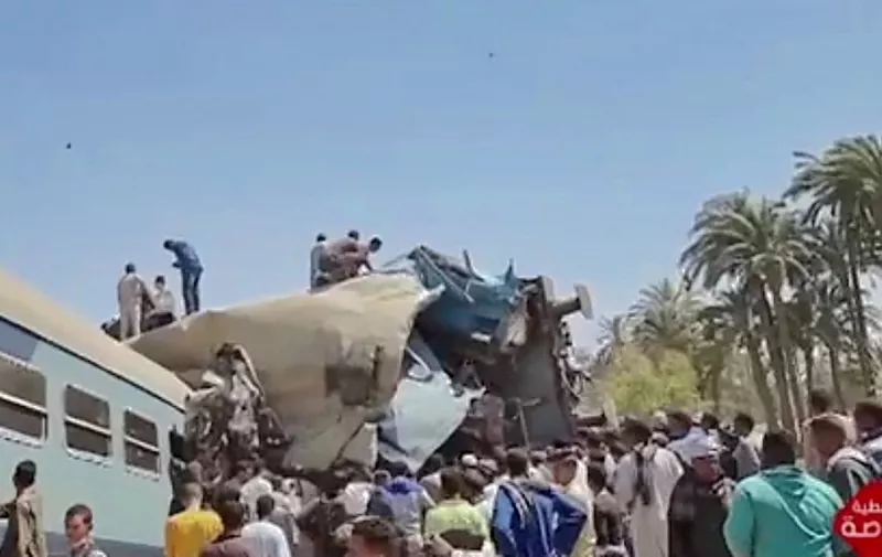 A video grab taken from the Egyptian state television station shows people gathered around two trains that collided in the Tahta district of Sohag province, some 460 kms (285 miles) south of the Egyptian capital Cairo, reportedly killing at least 32 people and injuring scores of others, on March 26, 2021. - Egypt has been plagued with deadly train accidents in recent years that have been widely blamed on inadequate infrastructure and poor maintenance. (Photo by STRINGER / EGYPTIAN STATE TV / AFP) / XGTY / RESTRICTED TO EDITORIAL USE - MANDATORY CREDIT "AFP PHOTO / EGYPTIAN TV " - NO MARKETING - NO ADVERTISING CAMPAIGNS - DISTRIBUTED AS A SERVICE TO CLIENTS