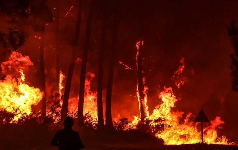 A silhouette is seen in front of flames at a wildfire near Belin-Beliet, southwestern France, overnight on August 11, 2022. - French officials warned that flare-ups could cause a massive wildfire to further spread in the country's parched southwest, where fresh blazes have already blackened swathes of land this week. Prime Minister is expected to meet with authorities battling the Landiras blaze south of Bordeaux, and further reinforcements are expected for the 1,100 firefighters on site, the prefecture of the Gironde department said. (Photo by Thibaud MORITZ / AFP)