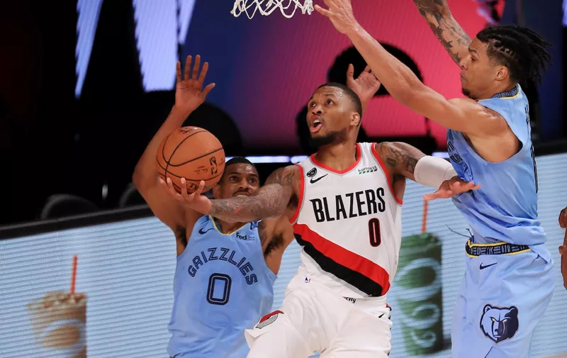 LAKE BUENA VISTA, FLORIDA - JULY 31: Damian Lillard #0 of the Portland Trail Blazers drives to the basket during the second half against De'Anthony Melton #0 and Brandon Clarke #15 of the Memphis Grizzlies at The Arena at ESPN Wide World Of Sports Complex on July 31, 2020 in Lake Buena Vista, Florida. NOTE TO USER: User expressly acknowledges and agrees that, by downloading and or using this photograph, User is consenting to the terms and conditions of the Getty Images License Agreement. (Photo by Mike Ehrmann/Getty Images)