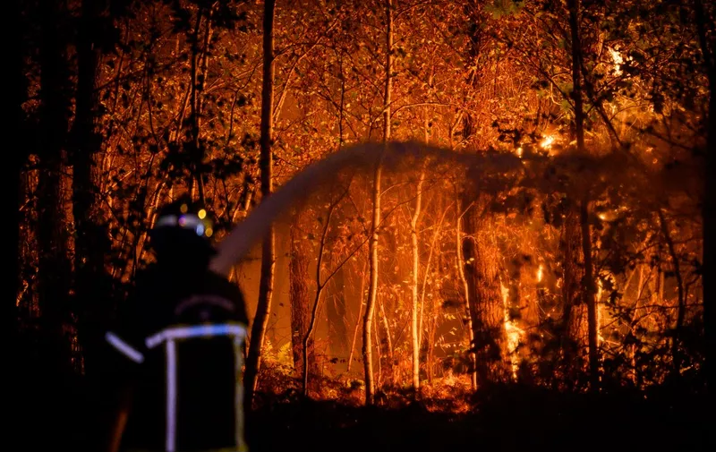 A firefighter sprays water towards flames at a night wildfire in Saumos on Bordeaux's western outskirts, southwestern France, on September 12, 2022. - A fire in progress since September 12, 2022 afternoon has covered between 320 and 350 hectares of vegetation and forest in Saumos and forced the evacuation of the town in a context of high temperatures in Gironde, firefighters said. (Photo by Philippe LOPEZ / AFP)
