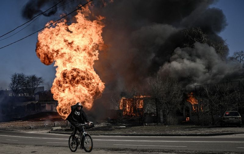 A cyclist rides past flames and smoke rising from a fire following an artillery fire on the 30th day of the invasion of Ukraine by Russian forces in the northeastern city of Kharkiv on March 25, 2022. - Russian strikes targeting a medical facility in Kharkiv on March 25, 2022, killed at least four civilians and wounded several others, Ukrainian officials said. (Photo by Aris Messinis / AFP)