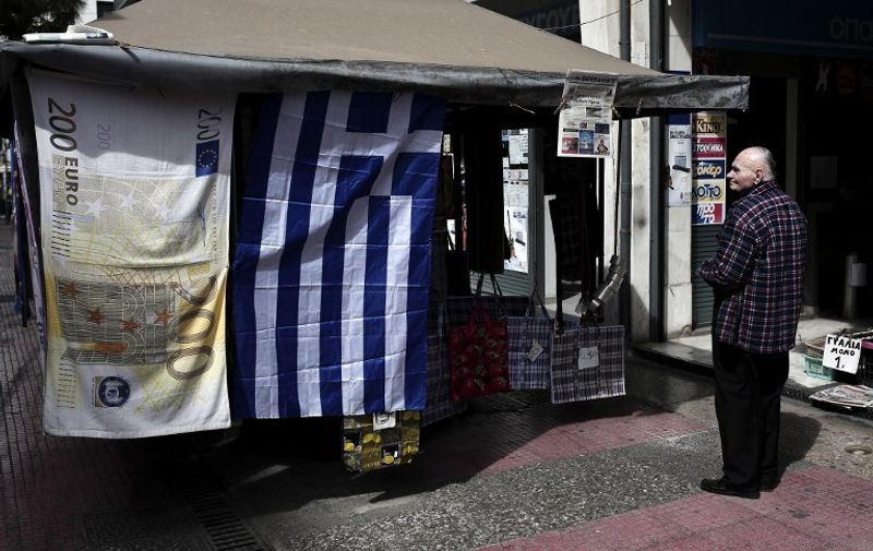 A man looks at the Greek flag (R) and a towel depicting a Euro banknote hanging outside a kiosk in Athens on March 22, 2015. The  German Chancellor Angela Merkel will receive Greece's radical left-wing Prime Minister Alexis Tsipras, who has blamed her insistence on tough austerity for his country's "humanitarian crisis" of poverty and mass unemployment. AFP PHOTO / Angelos Tzortzinis