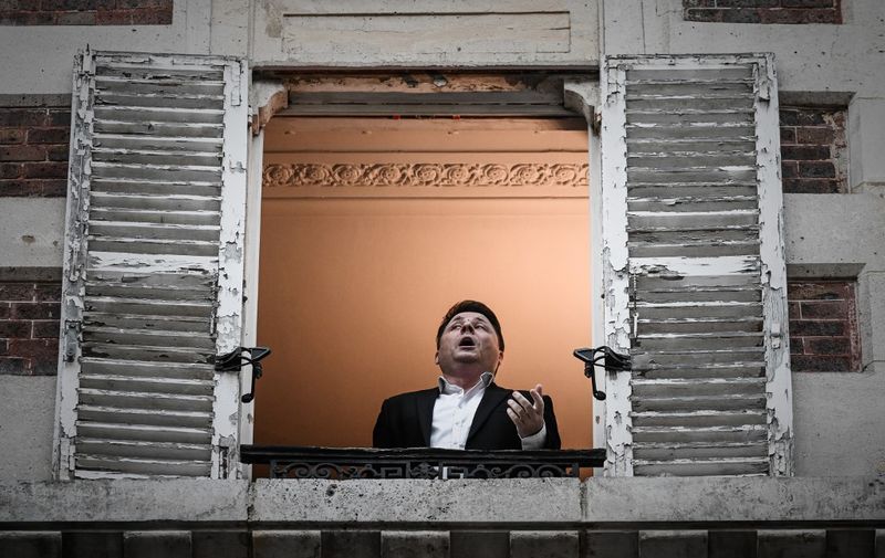 French opera tenor singer Stephane Senechal performs the song O sole mio from his window in Paris on March 26, 2020 on the evening of the tenth day of a strict lockdown in France aimed at curbing the spread of COVID-19, caused by the novel coronavirus. (Photo by PHILIPPE LOPEZ / AFP)