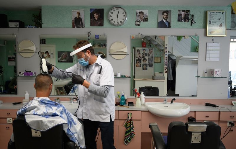 A hairdresser wearing a protective face mask and plastic gloves cuts the hair of a customer at Giaquinto hair salon after Switzerland started to ease the restrictions imposed to control the COVID-19 pandemic due to the novel coronavirus, on April 27, 2020 in Lausanne. - Doctors' surgeries, dentists, creches, hairdressers and massage and beauty salons were able to reopen, along with DIY stores, garden centres and florists. The Swiss stopped short of full confinement in emergency measures introduced last month to combat the spread of COVID-19. (Photo by Fabrice COFFRINI / AFP)