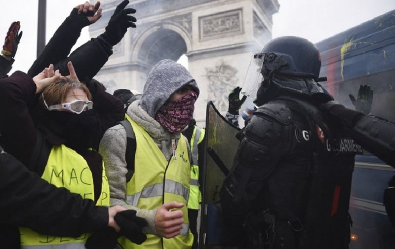 Demonstrators face riot police officers during a protest of Yellow vests (Gilets jaunes) against rising oil prices and living costs, near the Arc of Triomphe on the Champs Elysees avenue in Paris on December 1, 2018. - Thousands of anti-government protesters are expected today on the Champs-Elysees in Paris, a week after a violent demonstration on the famed avenue was marked by burning barricades and rampant vandalism that President Emmanuel Macron compared to "war scenes". (Photo by Lucas BARIOULET / AFP)