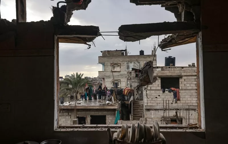 A picture taken through the window of a building damaged by Israeli bombing, shows members of a family standing on a rooftop, in Rafah in the southern Gaza Strip on January 27, 2024, as battles between Israel and the militant group Hamas continue. (Photo by AFP)