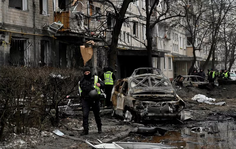 Police officers stand next to a destroyed car and a damaged residential building following a missile strike in Kyiv on December 13, 2023, amid Russian invasion of Ukraine. (Photo by SERGEI CHUZAVKOV / AFP)
