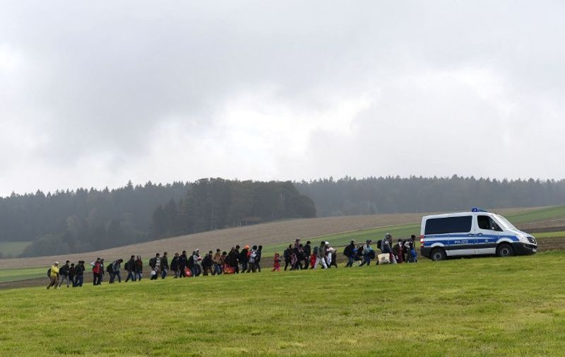 Migrants walk behind a police car during their way from the Austrian-German border to a first registration hall of the German federal police in the small Bavarian village Wegscheid, southern Germany, on October 20, 2015.  AFP PHOTO / CHRISTOF STACHE