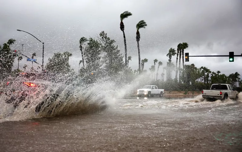 CATHEDRAL CITY, CALIFORNIA - AUGUST 20: Vehicles drive through a flooded street as Tropical Storm Hilary moves through the area on August 20, 2023 in Cathedral City, California. Southern California is under a first-ever tropical storm warning as Hilary impacts parts of California, Arizona and Nevada. All California state beaches have been closed in San Diego and Orange counties in preparation for the impacts from the storm, which was downgraded from hurricane status.   Mario Tama/Getty Images/AFP (Photo by MARIO TAMA / GETTY IMAGES NORTH AMERICA / Getty Images via AFP)