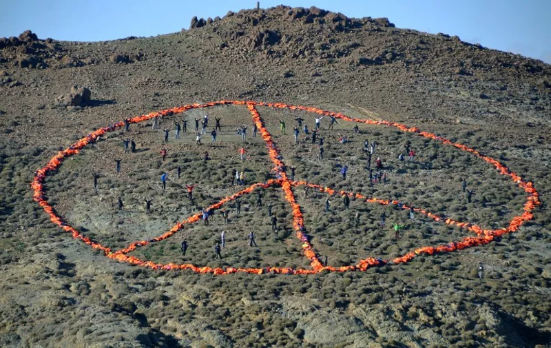 A handout photo released by Greenpeace and taken on New Year's Day, January 1, 2016 on the Greek island of Lesbos shows members of a Doctors without Borders (MSF) and Greenpeace team together with groups such as Sea-Watch, the Dutch Refugee Boat Foundation and local communities standing within a peace sign created from over 3,000 discarded refugee life jackets, calling for safe passage to those fleeing war, poverty and oppression.
More than one million migrants and refugees reached Europe in 2015, mainly fleeing violence in Afghanistan, Iraq and Syria, of whom four in five travelled via the Greek islands. / AFP / Greenpeace / FLORIAN SCHULZ / RESTRICTED TO EDITORIAL USE - MANDATORY CREDIT "AFP PHOTO / FLORIAN SCHULZ / MSF / GREENPEACE " - NO MARKETING NO ADVERTISING CAMPAIGNS - DISTRIBUTED AS A SERVICE TO CLIENTS - NO ARCHIVE