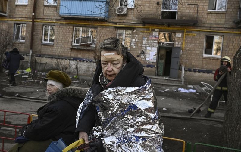 An injured woman looks on as she receives medical treatment after shelling in a residential area in Kyiv on March 18, 2022, as Russian troops try to encircle the Ukrainian capital as part of their slow-moving offensive. - Authorities in Kyiv said one person was killed early today when a downed Russian rocket struck a residential building in the capital's northern suburbs. They said a school and playground were also hit. (Photo by Aris Messinis / AFP)