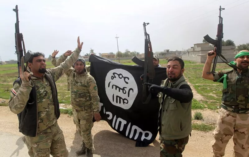 Members of the Iraqi paramilitary Popular Mobilisation units celebrate with a flag of the Islamic State (IS) group after retaking the village of Albu Ajil, near the city of Tikrit, from the jihadist group, on March 9, 2015. Some 30,000 Iraqi soldiers, police and the increasingly influential paramilitary Popular Mobilisation units, which are dominated by Shiite militias, have been involved in a week-old operation to recapture Tikrit, one of the jihadists' main hubs since they overran large parts of Iraq nine months ago.  AFP PHOTO / AHMAD AL-RUBAYE