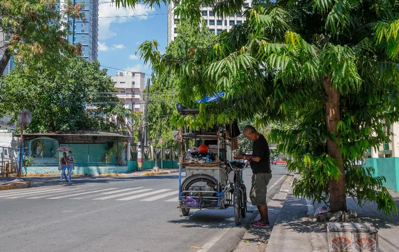 A vendor stands under a tree during hot weather in Manila on April 28, 2024. The Philippines will suspend in-person classes in all public schools for two days due to extreme heat and a nationwide strike by jeepney drivers, the education department said on April 28. (Photo by Earvin Perias / AFP)