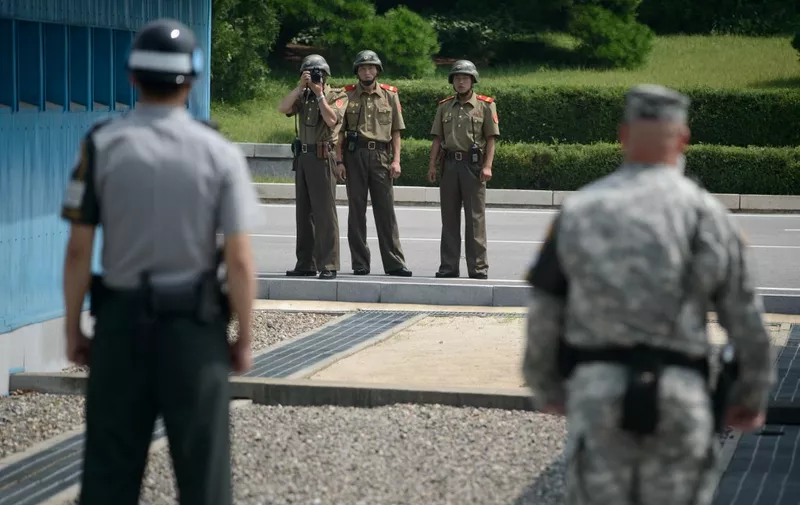 (FILES) North Korean soldiers (C) take photos towards a South Korean soldier (L) and a US soldier (R) standing before the military demarcation line (lower C) seperating North and South Korea within the Joint Security Area (JSA) at Panmunjom on July 27, 2014. A United States national entered North Korea during a tour of the heavily-fortified border and is believed to have been detained, the United Nations Command said July 18, 2023. (Photo by Ed JONES / AFP)