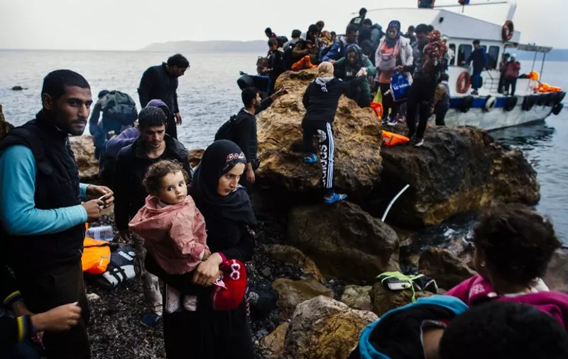 A woman holds a child on a beach shortly after arriving with other migrants and refugees on the Greek island of Lesbos after crossing the Aegean sea from Turkey on October 11, 2015. Greece pledged on October 10 during talks with its EU partners to open its first so-called hotspot reception centre on the island of Lesbos within 10 days under EU efforts to better deal with the massive influx of migrants. AFP PHOTO / DIMITAR DILKOFF