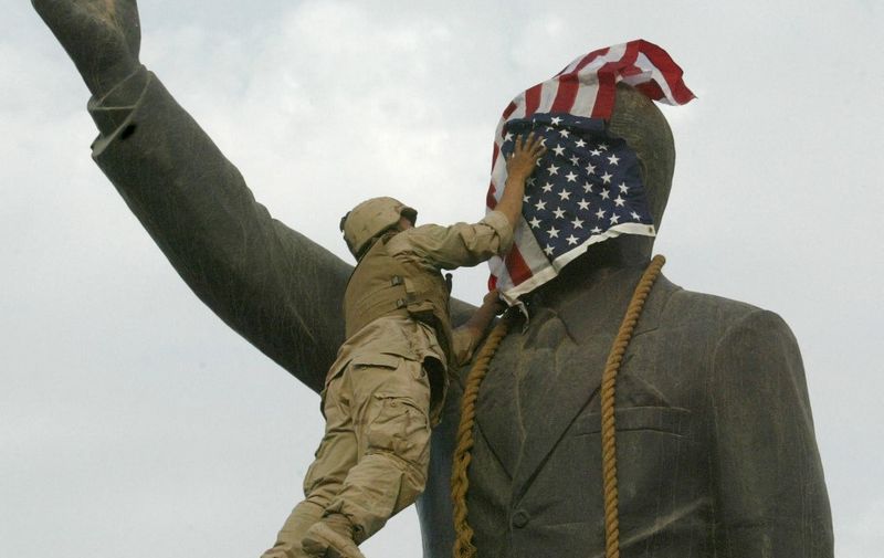 (FILES) In this file photo dated on April 9, 2003 a US Marine covers the face of Iraqi President Saddam Hussein's statue with the US flag in Baghdad's al-Fardous square. - Twenty years after the US-led invasion of Iraq toppled Saddam Hussein, the oil-rich country remains deeply scarred by the conflict and, while closer to the United States, far from the liberal democracy Washington had envisioned. (Photo by RAMZI HAIDAR / AFP)