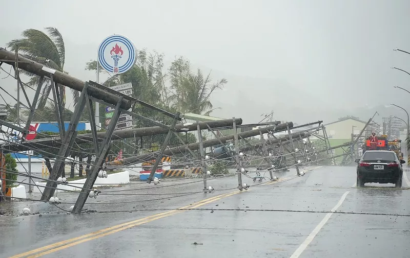 A car passes by power lines downed by the high winds from Typhoon Koinu in Taiwan's southern Pingtung County on October 5, 2023. Typhoon Koinu grazed the southern edge of Taiwan on October 5, blanketing the region in torrential rain and bringing record-breaking winds of more than 340 kilometres an hour to an outlying island. (Photo by Sean CHANG / AFP)