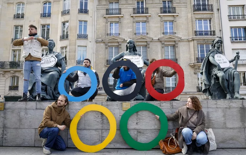 Activists of the collective "Le revers de la medaille" (the flip side of the coin) pose with olympic rings in front of statues next to the Orsay Museum in Paris, during a demonstration to draw attention to social inequality exacerbated by the upcoming Paris 2024 Olympic Games, on March 24, 2024. In what they refer to as "social cleansing" of the streets of Paris, the collective allege that the Olympic games will negatively impact those in need, including the homeless or people facing food insecurity. The placards read "2024 Olympic Games social cleaning legacy". (Photo by Geoffroy VAN DER HASSELT / AFP)