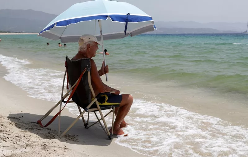 A man sits under the shade of a parasol on the Ricanto beach in Ajaccio, on the French island of Corsica, on July 19, 2023, as Europe is hit by a major heatwave. (Photo by Pascal POCHARD-CASABIANCA / AFP)