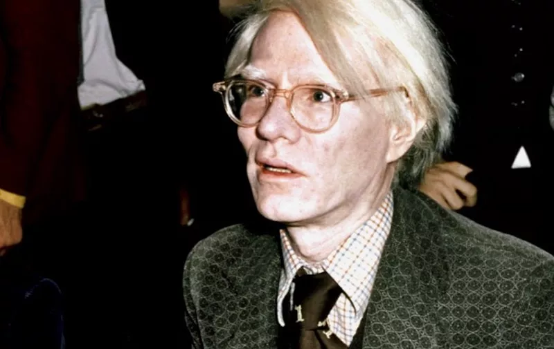 American pop artist and filmaker Andy Warhol signs copies of his book "From A t B and back again" in London, November 1975. (Photo by AP / AFP)