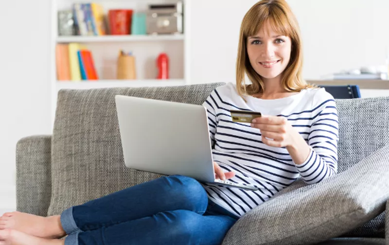 Mid adult woman shopping using laptop and credit card in modern apartment. Ecommerce