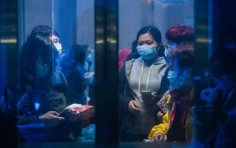 A man (2L) wearing a facemask as a preventative measure following a coronavirus outbreak which began in the Chinese city of Wuhan, waits outside the glass doors of an elevator as he holds a newly purchased box of face masks after he and thousands of others lined up to buy them in Hong Kong on February 5, 2020. - The new coronavirus which appeared late December has claimed nearly 500 lives, infected more than 24,000 people in mainland China and spread to more than 20 countries. (Photo by Anthony WALLACE / AFP)