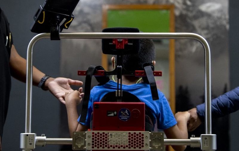 David Zabala, an 8-year-old boy with cerebral palsy, is assisted by a physical therapist and his mother, Guadalupe Cardozo Ruiz (R), during a rehabilitation session with the robotic exoskeleton Atlas 2030 at the Association for People with Cerebral Palsy (APAC) in Mexico City on October 18, 2022. - The Atlas 2030 pediatric exoskeleton, which won its creator, Spanish Elena GarcÌa Armada, the 2022 European Inventor award, has been in use in Mexico since October, thanks to the efforts of the Association for People with Cerebral Palsy (APAC), a private organisation founded in 1970. (Photo by CLAUDIO CRUZ / AFP)