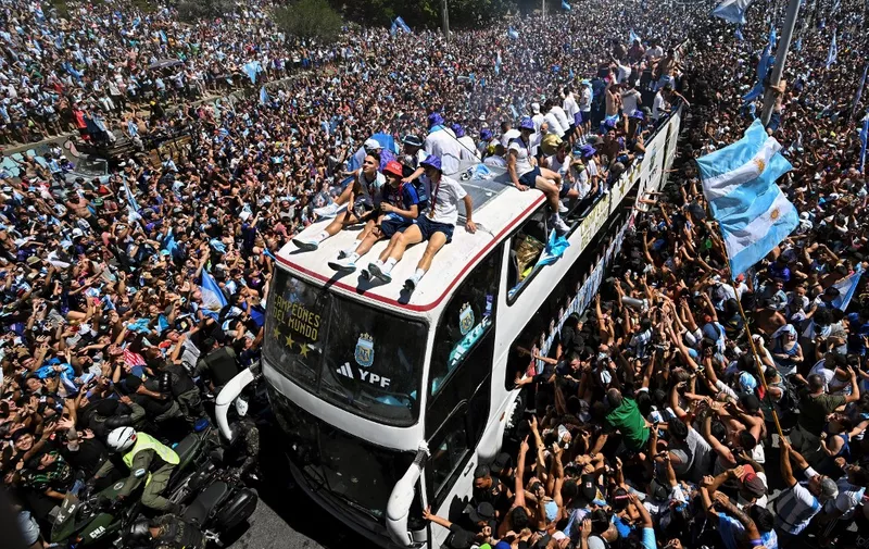 Fans of Argentina cheer as the team parades on board a bus after winning the Qatar 2022 World Cup tournament in Buenos Aires, Argentina on December 20, 2022. - Millions of ecstatic fans are expected to cheer on their heroes as Argentina's World Cup winners led by captain Lionel Messi began their open-top bus parade of the capital Buenos Aires on Tuesday following their sensational victory over France. (Photo by Luis ROBAYO / AFP)