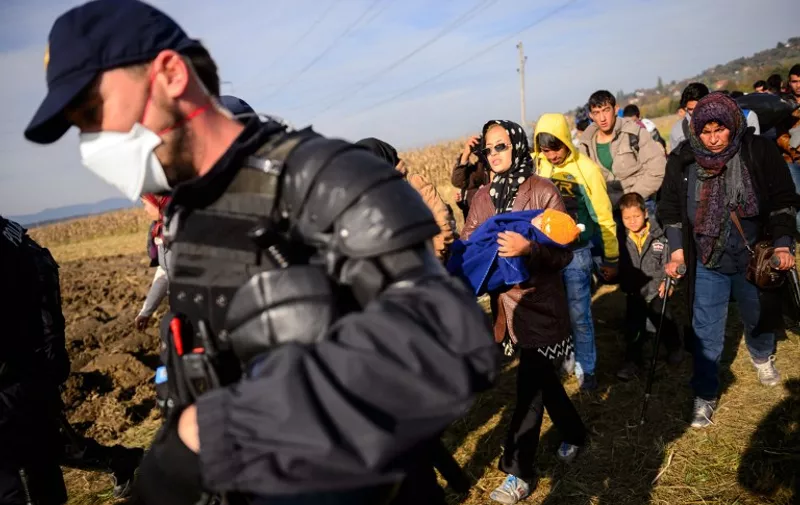 A woman carries an infant wrapped in a blanket as migrants and refugees walk through a field escorted by police officers to a refugee center after crossing the Croatian-Slovenian border near Rigonce, Slovenia, on October 25, 2015. The European Union will "start falling apart" if it fails to take concrete action to tackle the migrant crisis within the next few weeks, Slovenian Prime Minister Miro Cerar warned on October 25. AFP PHOTO / JURE MAKOVEC