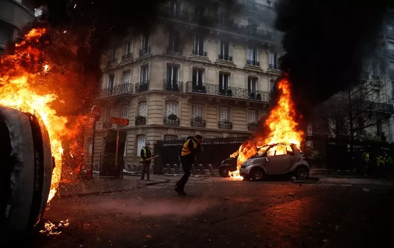Protesters walk by burning cars during clashes with riot police on the sideline of a protest of Yellow vests (Gilets jaunes) against rising oil prices and living costs, on December 1, 2018 in Paris. (Photo by Abdulmonam EASSA / AFP)