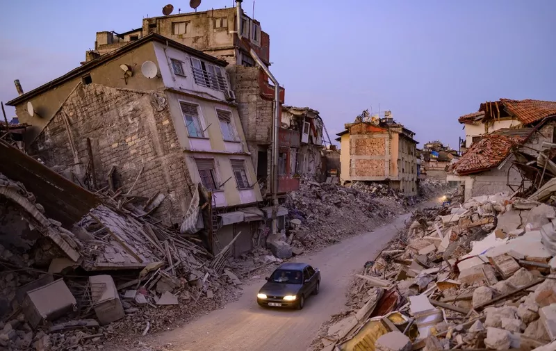 A car drives past collapsed buildings in Antakya, southern Turkey on February 20, 2023. - A 7.8-magnitude earthquake hit near Gaziantep, Turkey, in the early hours of February 6, followed by another 7.5-magnitude tremor just after midday. The quakes caused widespread destruction in southern Turkey and northern Syria and has killed more than 44,000 people. (Photo by Yasin AKGUL / AFP)