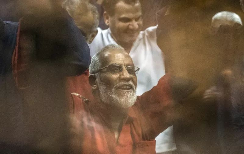 Egyptian Muslim Brotherhood leader Mohamed Badie (C) raises his hands from behind the defendant's cage as the judge reads out the verdict sentencing him and more than 100 other defendants, including Egypt's deposed Islamist president Mohamed Morsi, to death at the police academy in Cairo on May 16, 2015. AFP PHOTO / KHALED DESOUKI