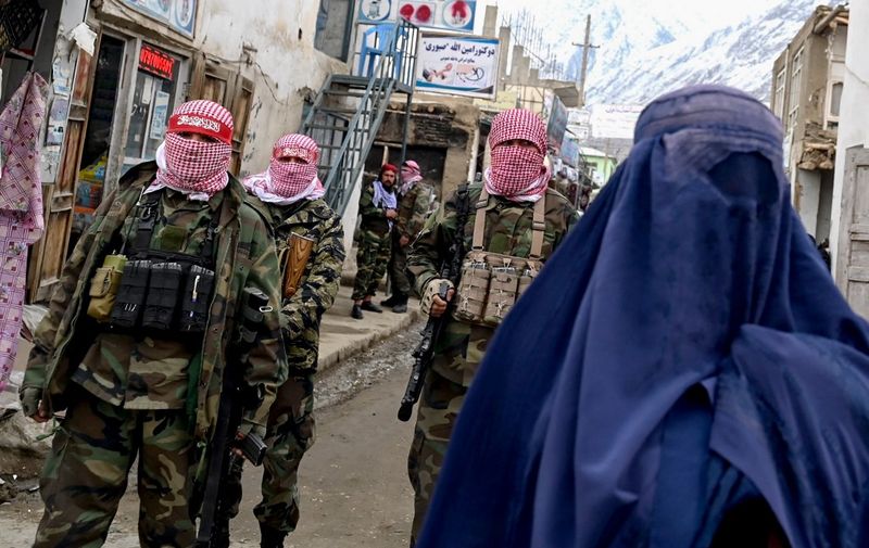 Taliban security personnel stand guard as an Afghan burqa-clad woman (R) walks along a street at a market in the Baharak district of Badakhshan province on February 26, 2024. (Photo by Wakil KOHSAR / AFP)