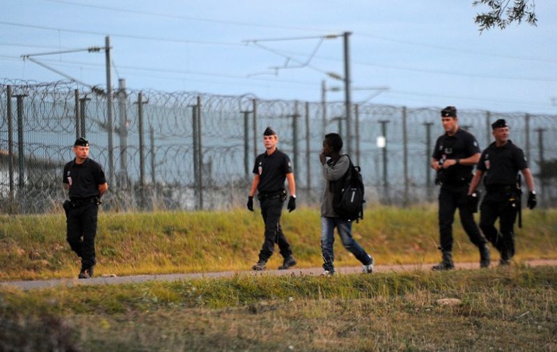 Police officers follow a young migrant in Coquelles near the northern French port of Calais as part of security efforts to stop migrants from reaching the Eurotunnel terminal on August 3, 2015. Migrants in Calais made around 1,700 attempts overnight to penetrate the Channel Tunnel premises in a bid to get to England, French police sources said, and an officer sustained facial injuries from a stone. Of the 1,700 attempts, some 1,000 were "pushed back" by authorities and 700 were intercepted within the 650-hectare Channel Tunnel site, police added. AFP PHOTO / FRANCOIS LO PRESTI