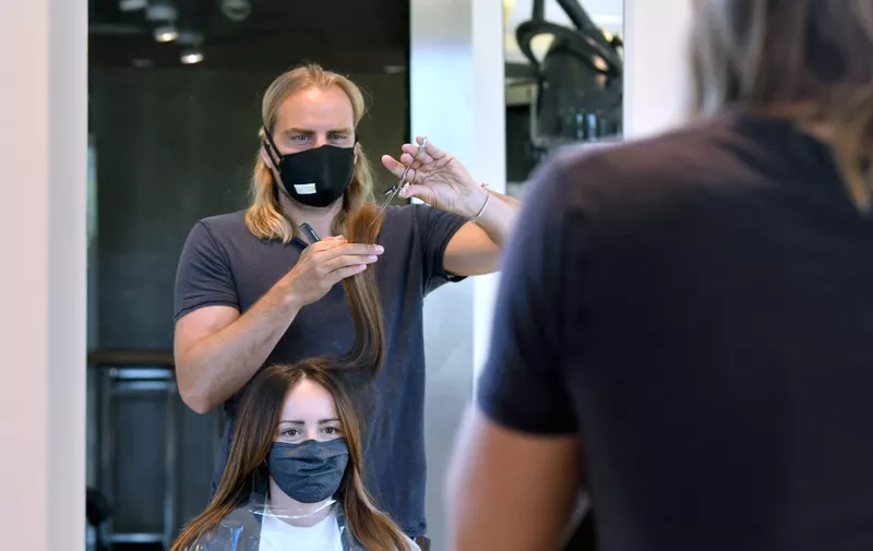 A hairdresser cuts the hair of a customer, both wearing protective masks in Salzburg, Austria on May 2, 2020. - Austrian citizens are allowed to leave the house for non-essential trips as it eases coronavirus lockdown measures, but said limits on gatherings and social distancing rules would remain in place. From May 2, 2020, shopping centres, hairdressers and all shops with more than 400 square metres of sales area are allowed to reopen, including the major electrical retailers, fashion chains, furniture stores and sports equipment retailers. (Photo by BARBARA GINDL / APA / AFP) / Austria OUT