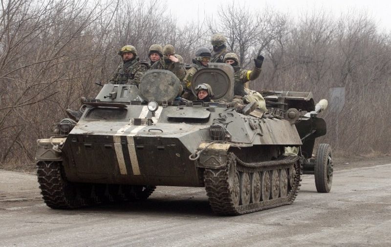 Soldiers gesture as an Ukrainian Armoured Personnel Carrier move a cannon from a position near eastern Ukrainian city of Artemivsk, in the Donetsk region on February 26, 2015. The Ukraine's military said it was starting the withdrawal of heavy weapons from the frontline with pro-Russian rebels, a key step in a stuttering peace plan. "Ukraine is beginning the withdrawal of 100mm cannons from the frontline. This is the first step in the pull-back of heavy weapons," the military said in a statement. AFP PHOTO/ ANATOLII STEPANOV