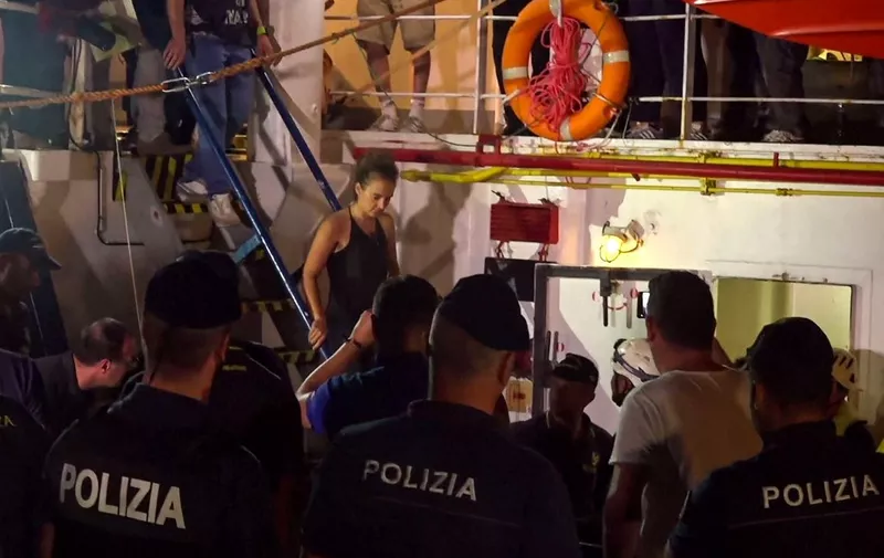 An image grab taken from a video released by Local Team on June 29, 2019, shows the Sea-Watch 3 charity ship's German captain Carola Rackete being arrested by Italian police, in the Italian port of Lampedusa, Sicily. - The Sea-Watch 3 charity ship carrying dozens of migrants rescued off Libya forced its way into the Italian port of Lampedusa on June 28 night after a lengthy standoff, the charity said. The boat's German captain Carola Rackete, 31, was arrested and the 40 migrants were still on board after the vessel docked. After manoeuvring the ship into port without permission, Rackete was arrested by police for refusing to obey a military vessel, a crime punishable by between three and 10 years in jail. She offered no resistance and was escorted off the vessel without  handcuffs. (Photo by Anaelle LE BOUEDEC / various sources / AFP) / Italy OUT