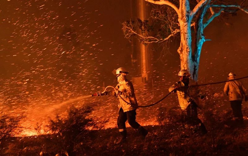 This picture taken on December 31, 2019 shows firefighters hosing down embers to secure nearby houses from bushfires near the town of Nowra in the Australian state of New South Wales. (Photo by SAEED KHAN / AFP)