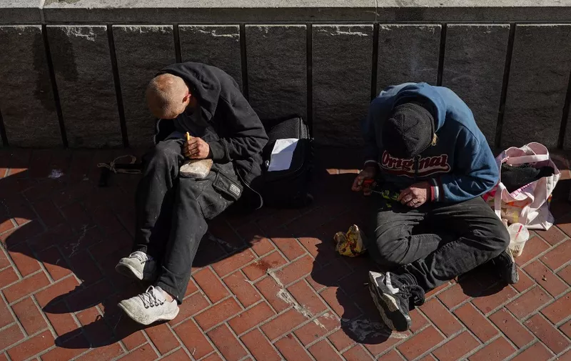 Homeless people sit against a public transit station wall near APEC Summit headquarters on November 11, 2023 in downtown San Francisco, California. The city took steps to clean up in advance of the APEC Summit, currently taking place through November 17. (Photo by Loren Elliott / AFP)