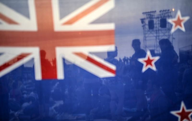 (FILES) In this file picture taken on April 24, 2014, people are seen behind a New Zealand flag as they wait for the dawn ceremony in the Anzac cove during the ceremony celebrating the 99th anniversary of the Anzac Day in Canakkale. New Zealanders began voting on November 20, 2015 to select a potential new flag, as the South Pacific country considers dropping Britain's Union Jack from its national banner.  AFP PHOTO / FILES / BULENT KILIC / AFP / BULENT KILIC