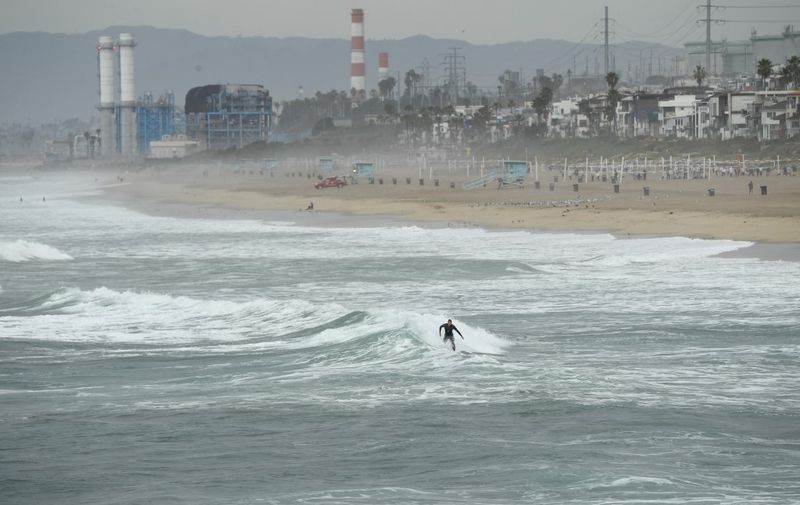 A surfer catches a wave in Manhattan Beach, California, on January 15, 2022. - The US National Weather Service issued tsunami advisories for the entire west coast of the United States following a massive volcanic eruption across the Pacific Ocean in Tonga. (Photo by Patrick T. FALLON / AFP)