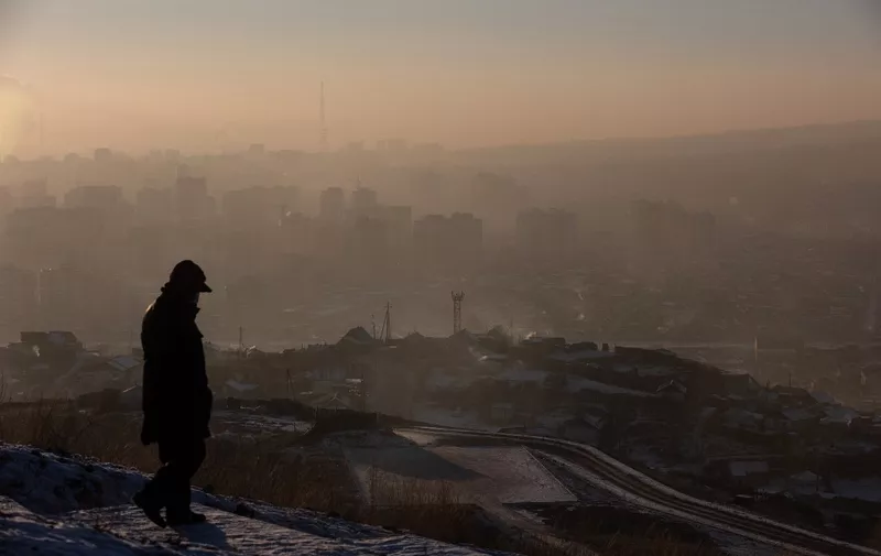 This picture taken on January 16, 2022 shows a man watching smoke hanging over houses on a polluted day in Ulaanbaatar, the capital of Mongolia. (Photo by BYAMBASUREN BYAMBA-OCHIR / AFP)