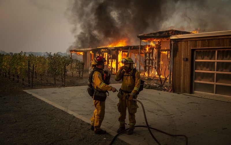 Firefighters discuss how to approach the scene as a home burns near grape vines during the Kincade fire in Healdsburg, California on October 27, 2019. - Powerful winds were fanning wildfires in northern California in "potentially historic fire" conditions, authorities said October 27, as tens of thousands of people were ordered to evacuate and sweeping power cuts began in the US state. (Photo by Josh Edelson / AFP)
