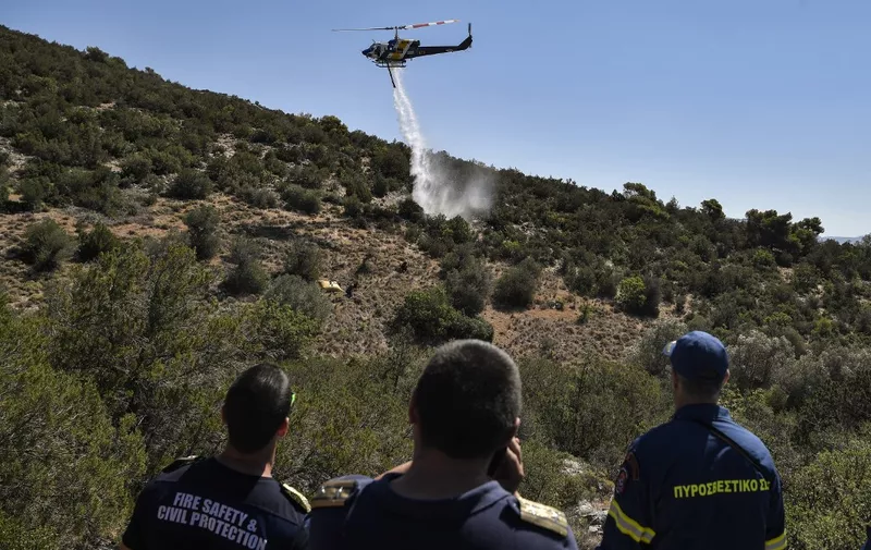 Chiefs of teams of the EU-funded Rescue firefighters mission watch an Augusta firefighting helicopter dropping water during a training session to prevent and fight wildfires, in Magoula central Greece, on June 30, 2022. - In Magoula, on the outskirts of Athens, on a plot of land that still bears the traces of last summer's fires, a team of European firefighters is training with their Greek counterparts to prepare for the fire season and avoid the worst. (Photo by Louisa GOULIAMAKI / AFP)