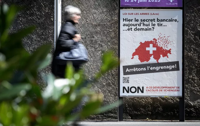 A woman walks past a campaign poster against toughening gun law in Switzerland and reading in French "Yesterday banking secrecy, today shooting... and tomorrow ? Let's stop the spiral!", on May 13, 2019, in Geneva. - The Swiss will vote on May 19 on whether to bring the country's gun laws in line with EU legislation, with the government warning a 'no' could threaten relations with the bloc. A demand from the neighbouring European Union that Switzerland toughen its gun laws has prompted a rare national debate over firearm ownership in the wealthy Alpine nation, which has a deeply-rooted gun culture. (Photo by Fabrice COFFRINI / AFP)